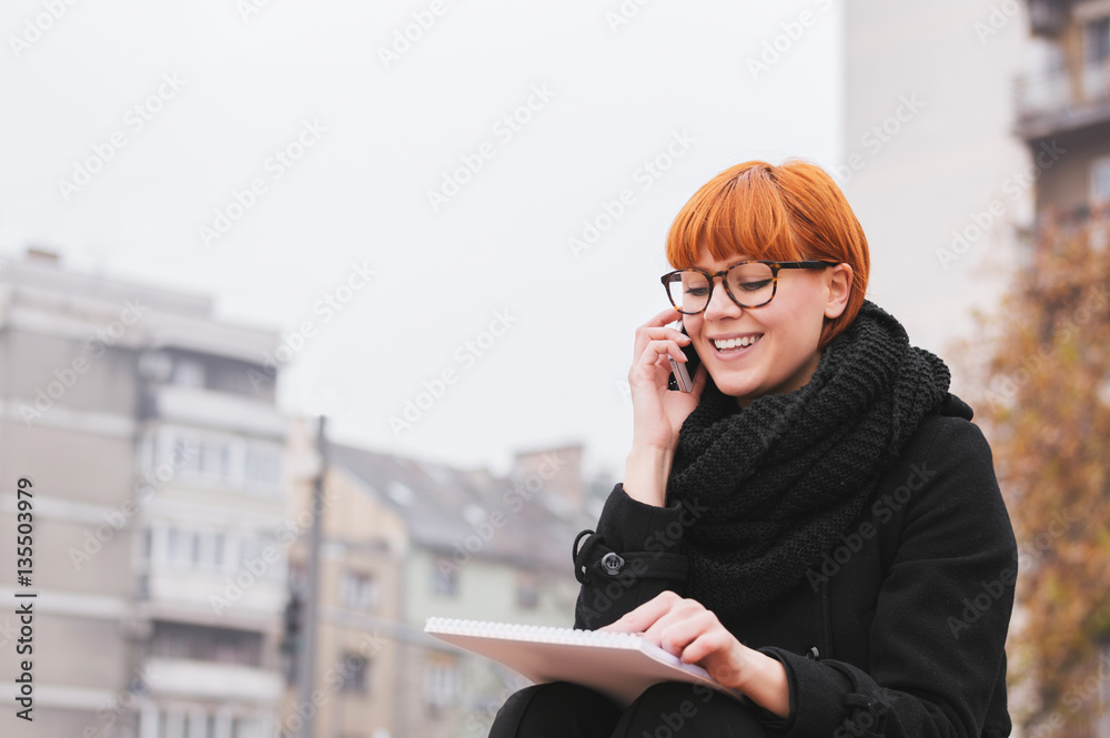 Happy young lady talking on mobile phone on the street