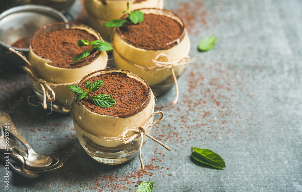 Homemade Italian dessert Tiramisu served in individual glasses with mint leaves and cocoa powder ove