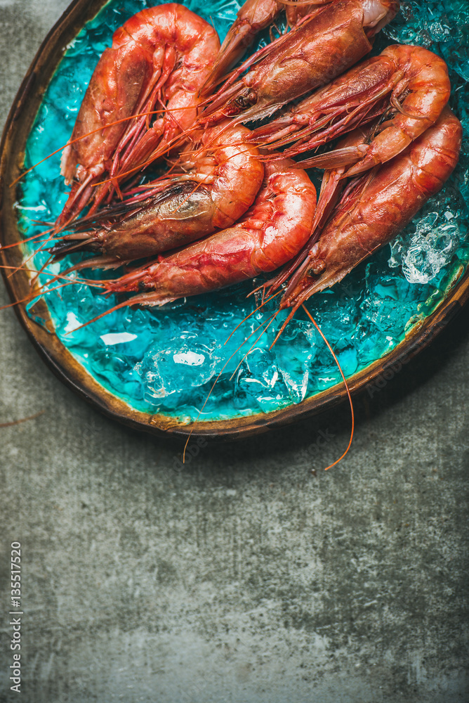 Raw uncooked red shrimps on chipped ice in turquoise blue ceramic tray over grey concrete background