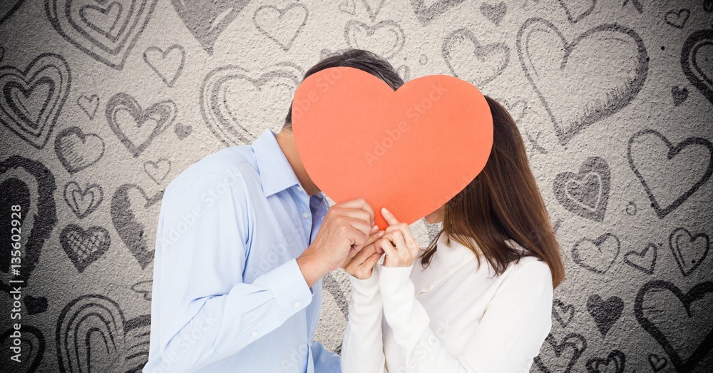 Romantic couple hiding their face behind red heart