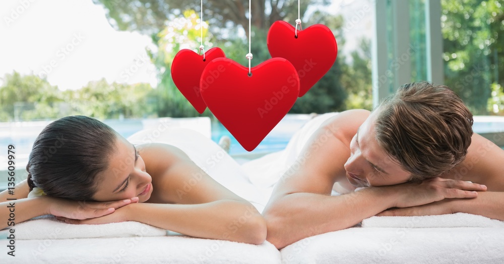 Composite image of hanging red heart and couple lying at spa