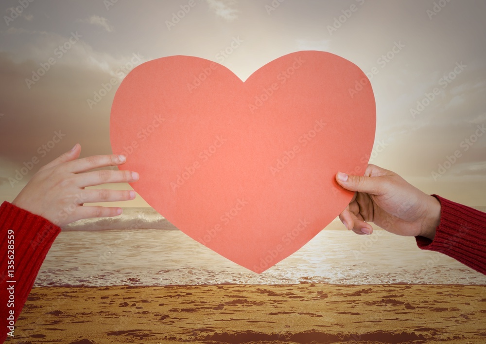 Hand of couple holding red heart on beach