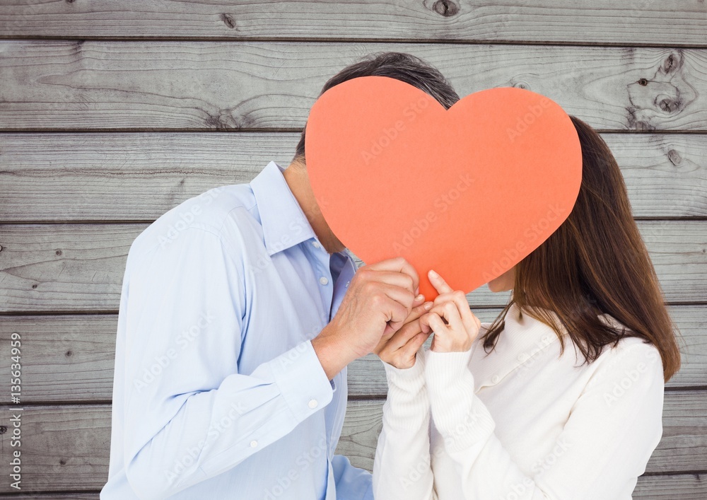 Romantic couple hiding their face behind heart