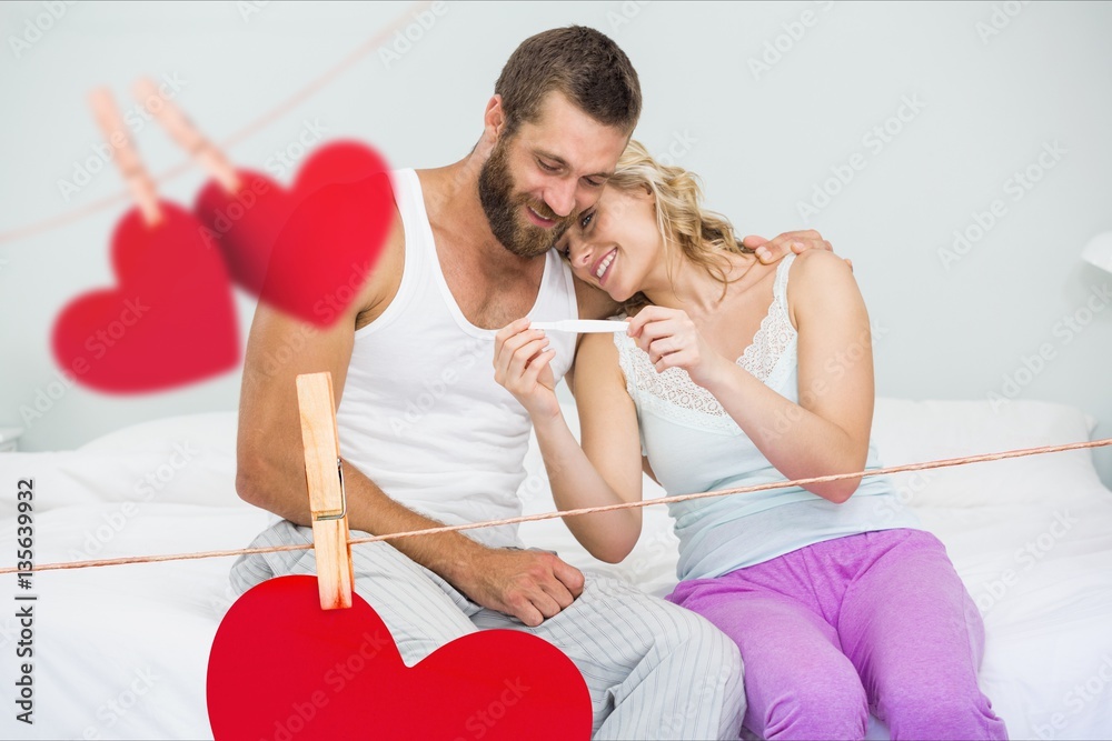 Romantic couple looking at pregnancy test in bedroom at home