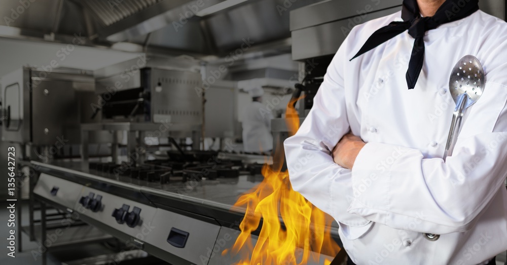 Mid section of chef standing with arms crossed in kitchen