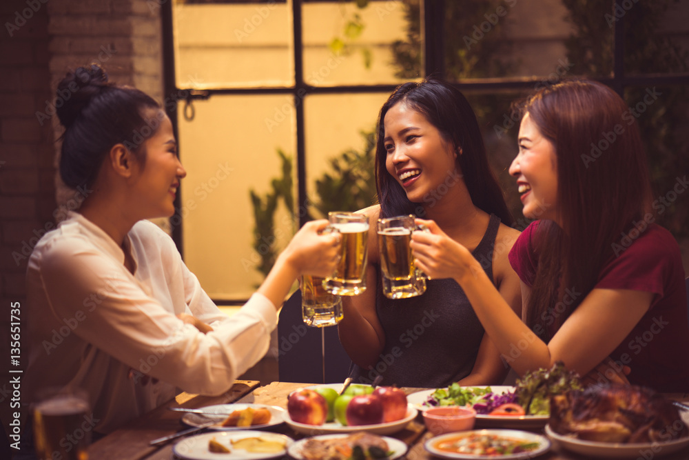 Women are drinking beer and the clink glasses in a restaurant.