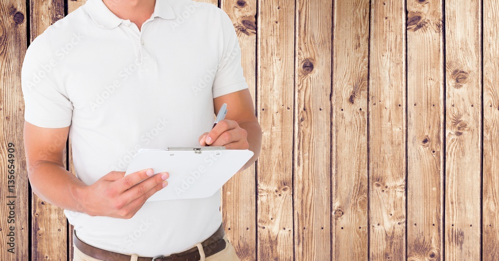 Delivery man writing on clipboard against wooden background