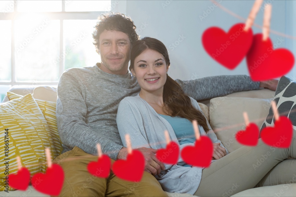 Composite image of red heart and couple embracing on sofa