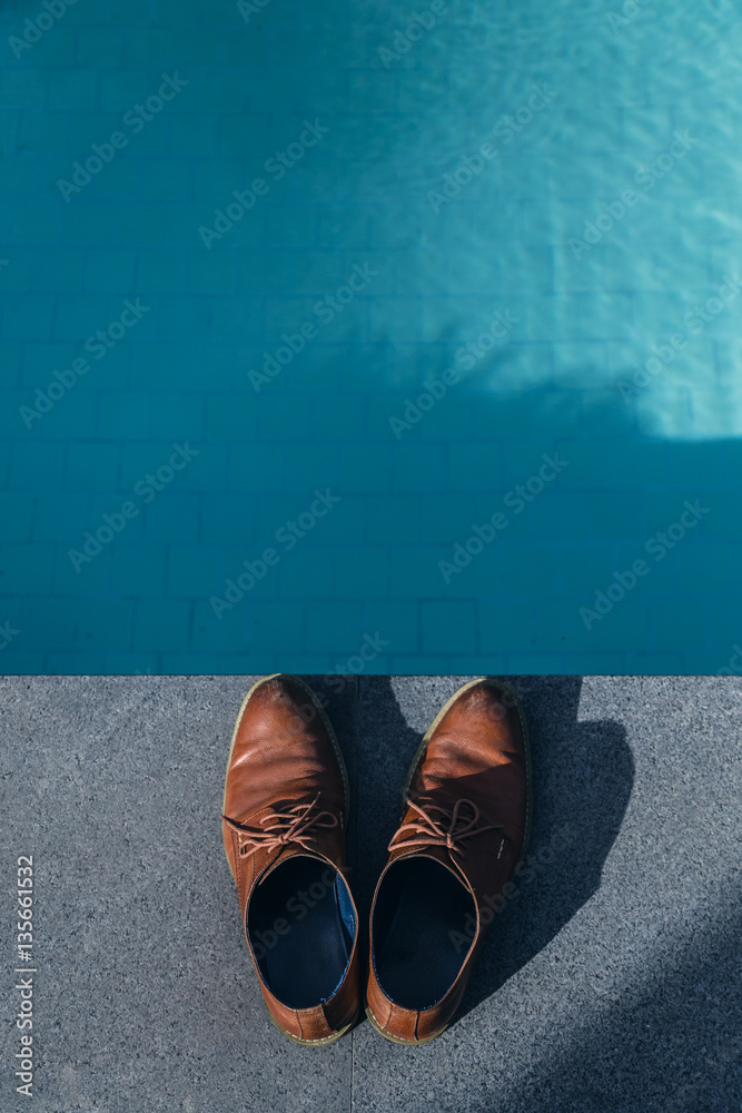 man brown leather shoe with blue jeans on terrace near swiming p