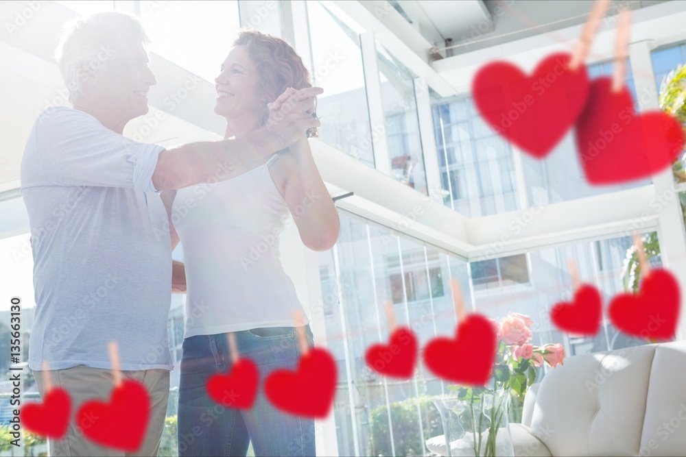 Composite image of hanging red hearts and mature couple dancing