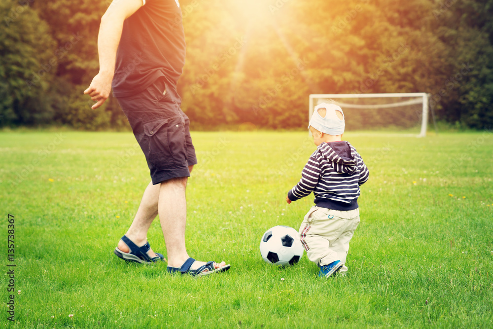 Little boy playing football on the field with gates