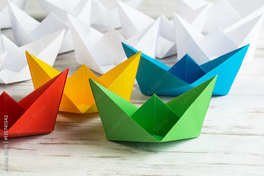 Business leadership concept with white and color paper boats on wooden table