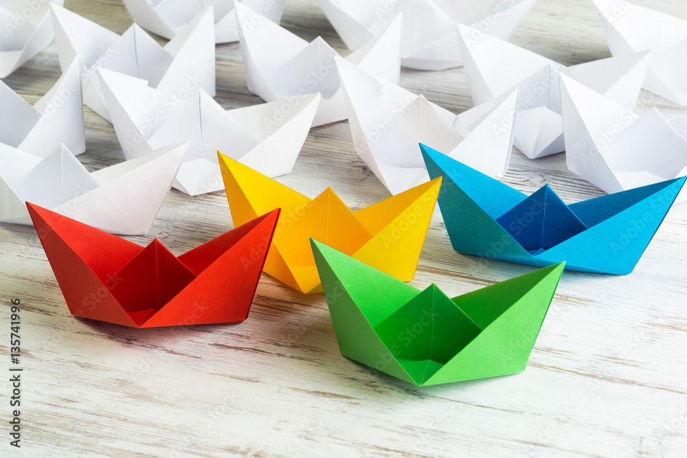 Business leadership concept with white and color paper boats on wooden table