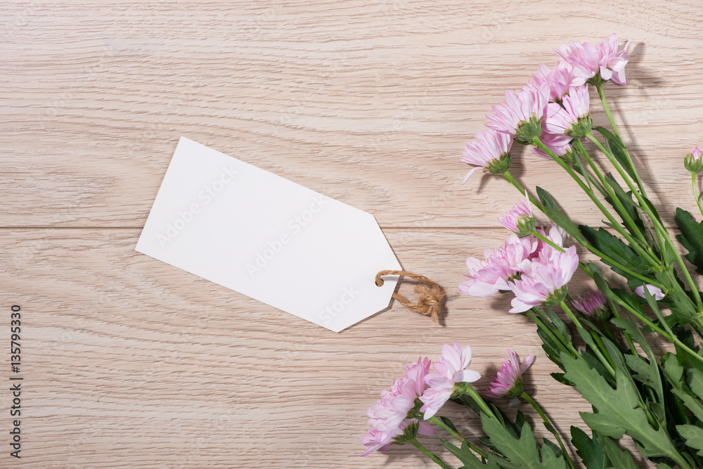 Blank white tag paper with color flowers on wooden background. T