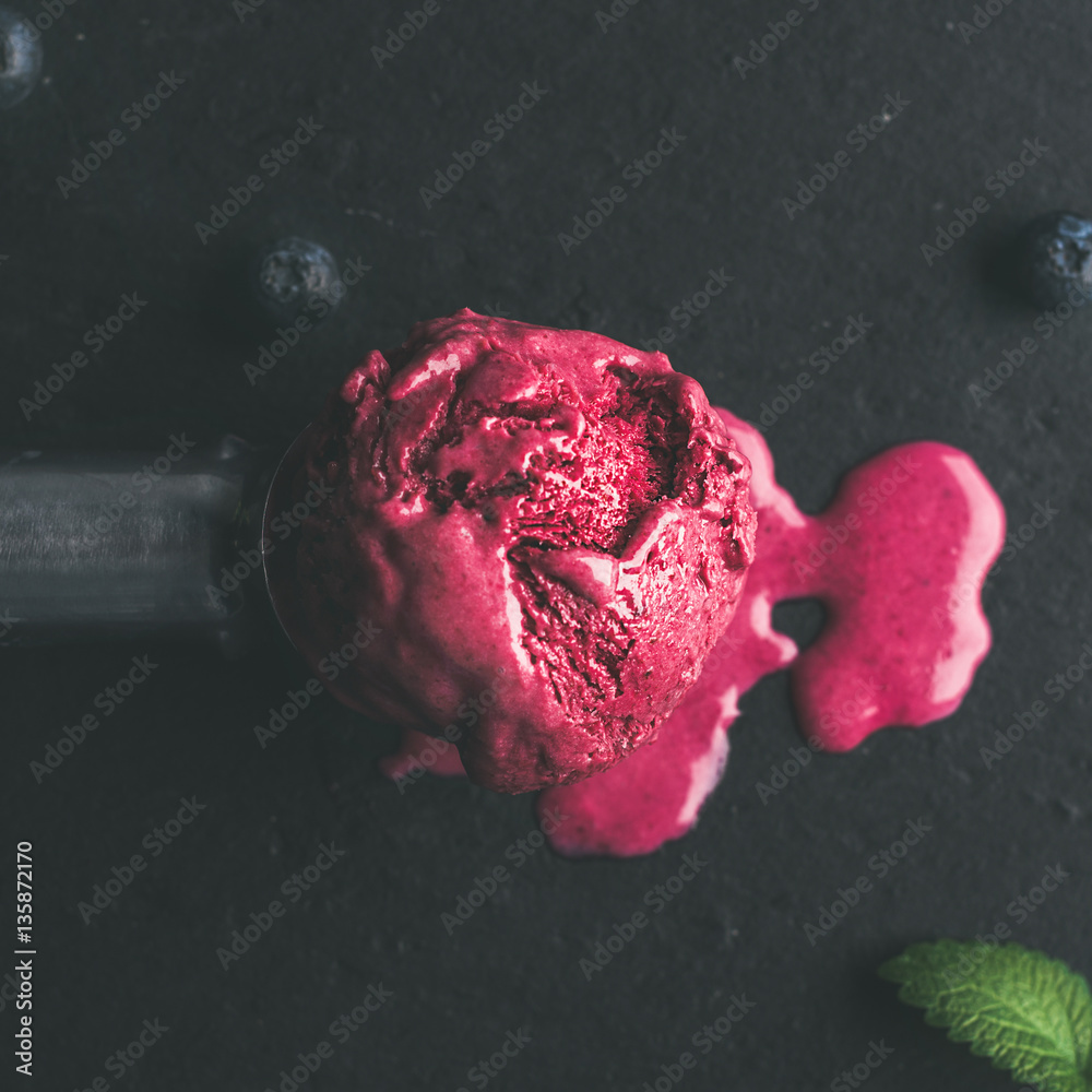 Melting scoop of blueberry ice-cream with mint leaves over black slate stone background, top view, s