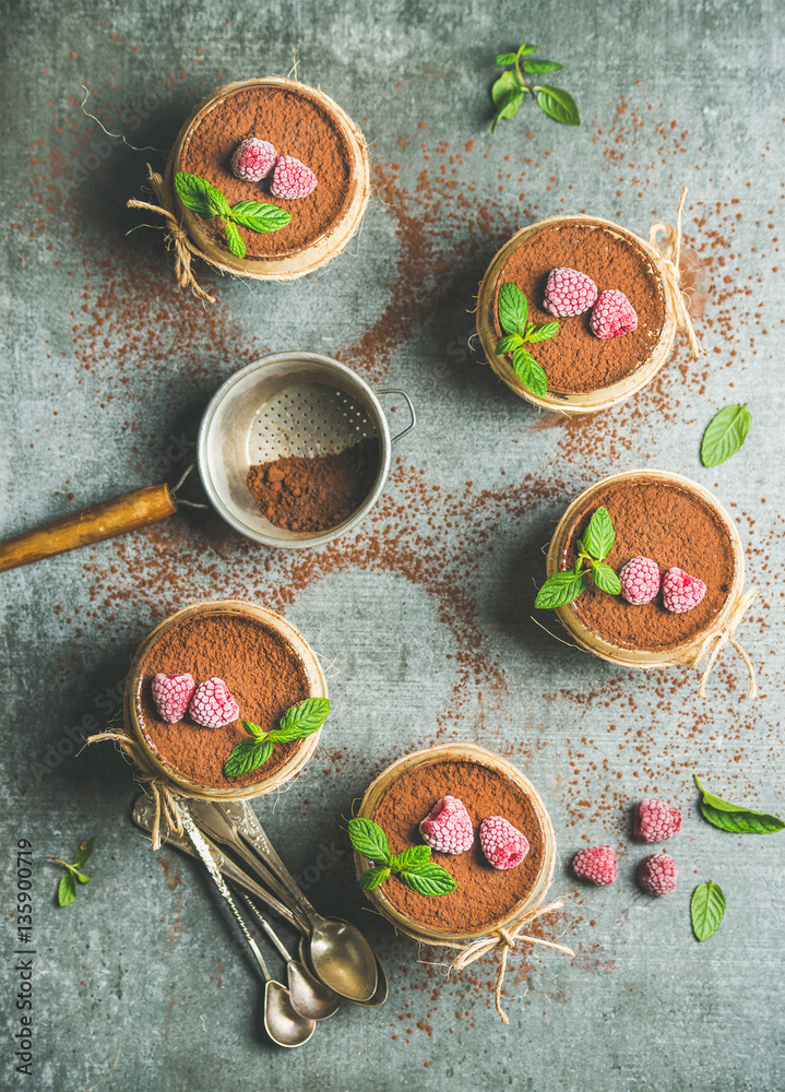 Homemade Italian dessert Tiramisu served in individual glasses with mint leaves, raspberries and coc