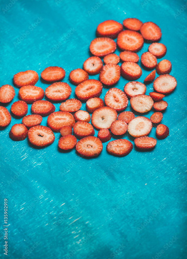 Pieces of fresh strawberries in shape of heart on bright blue painted background, selective focus, c