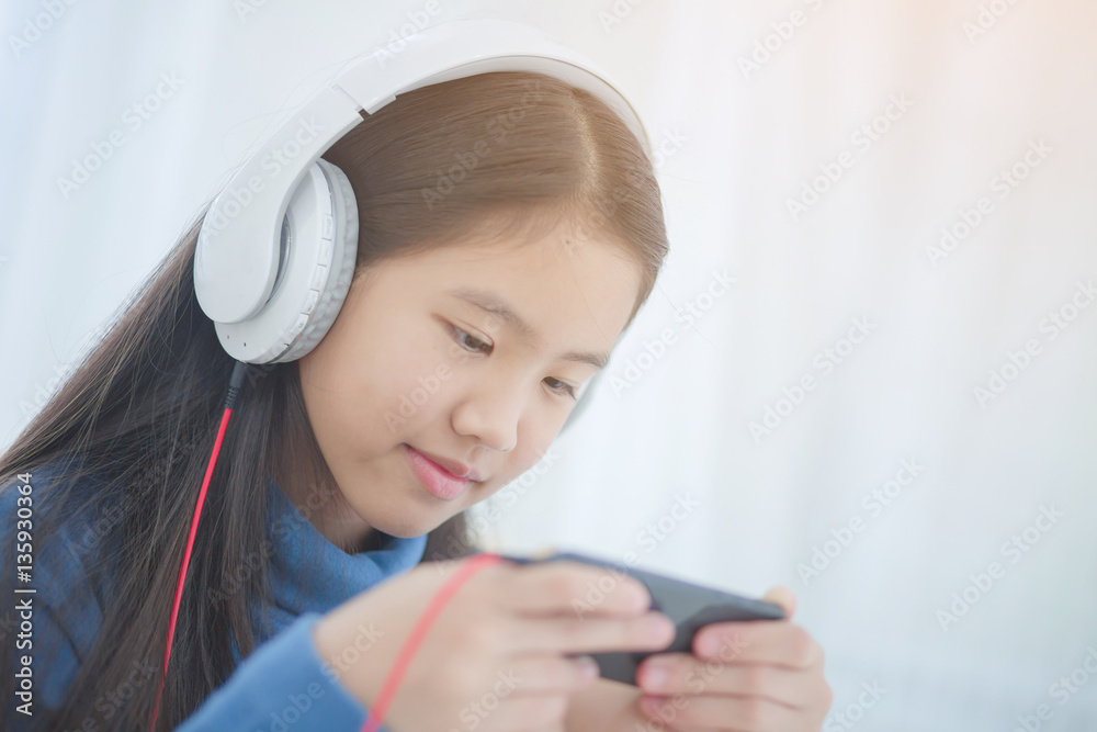 Pretty Asian girl using headphone for listen music by smartphone on the bed in her bedroom