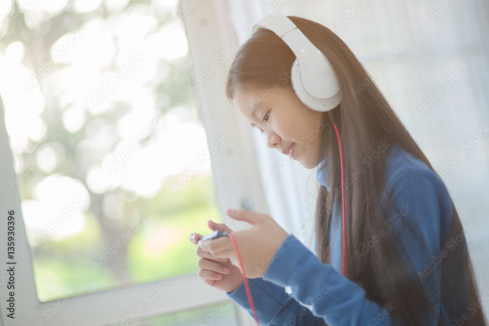 Pretty Asian girl using headphone for listen music by smartphone on the bed in her bedroom