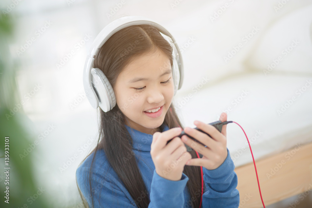 Pretty Asian girl using headphone for listen music by smartphone on the bed in her bedroom