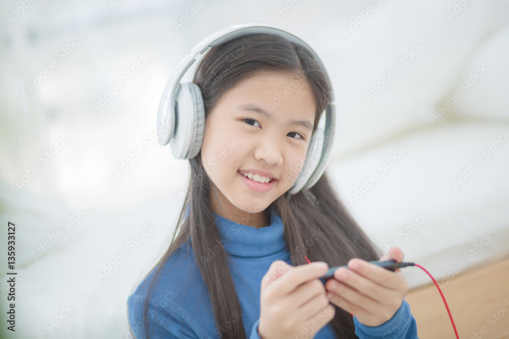 Pretty Asian girl using headphone for listen music by smartphone on the bed in her bedroom