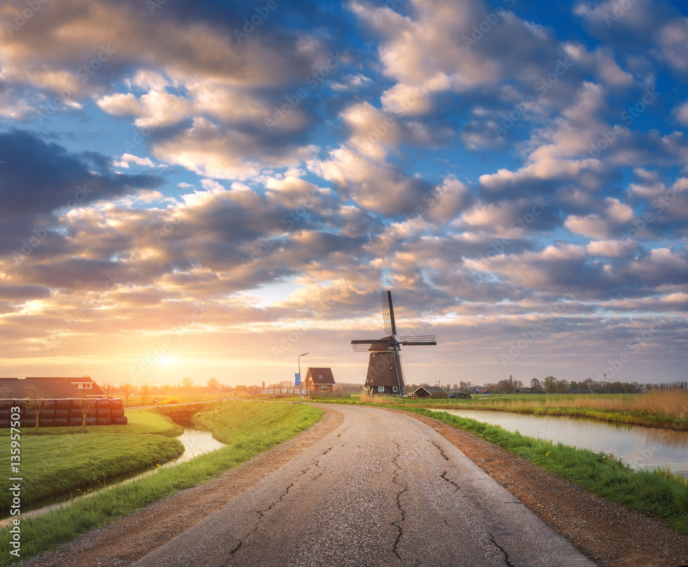 Road with windmill at sunrise in Netherlands. Traditional dutch windmill against colorful sky with c