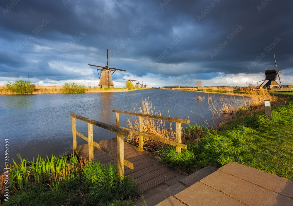 Windmills at sunset in Kinderdijk, Netherlands. Rustic landscape with wooden pier against traditiona