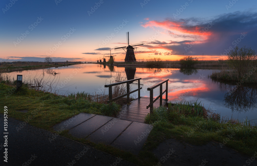 Silhouette of windmills at sunrise in Kinderdijk, Netherlands. Rustic landscape with wooden pier aga