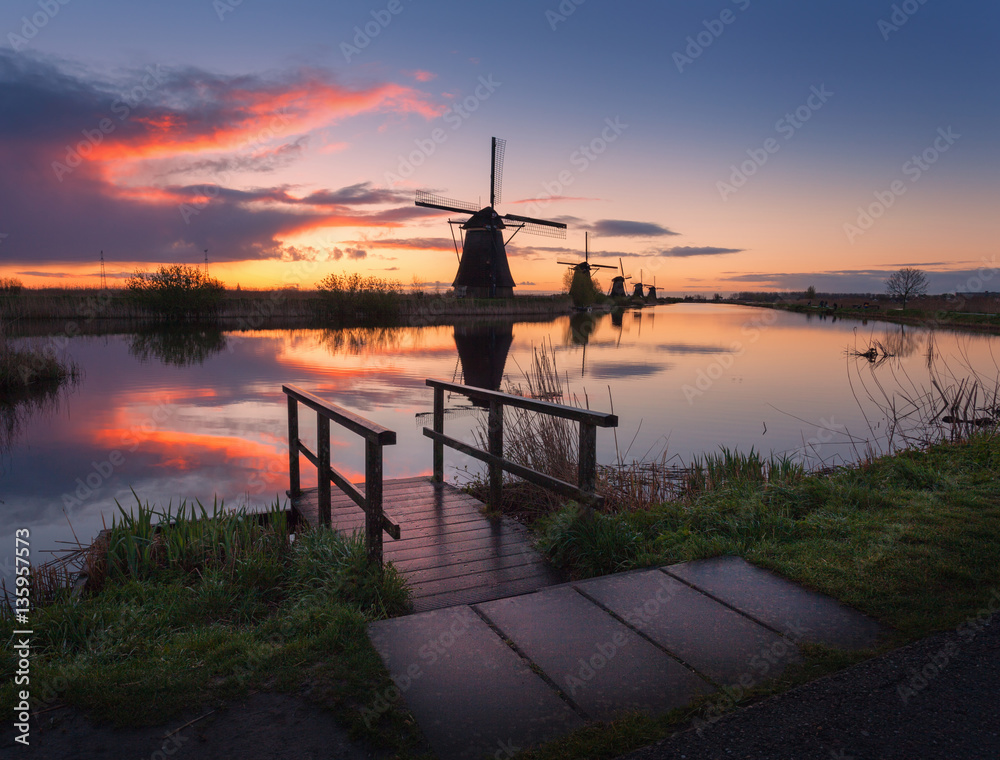 Silhouette of windmills at sunrise in Kinderdijk, Netherlands. Rustic landscape with wooden pier aga