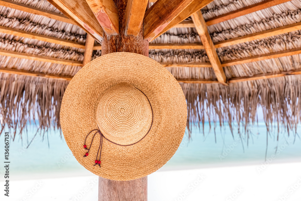 Sun hat hanging on sunshade umbrella on tropical beach. Maldives.