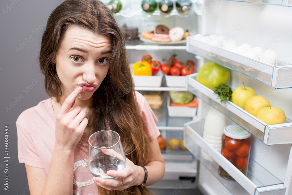 Portrait of a young thinking woman in front of the refrigerator full of food