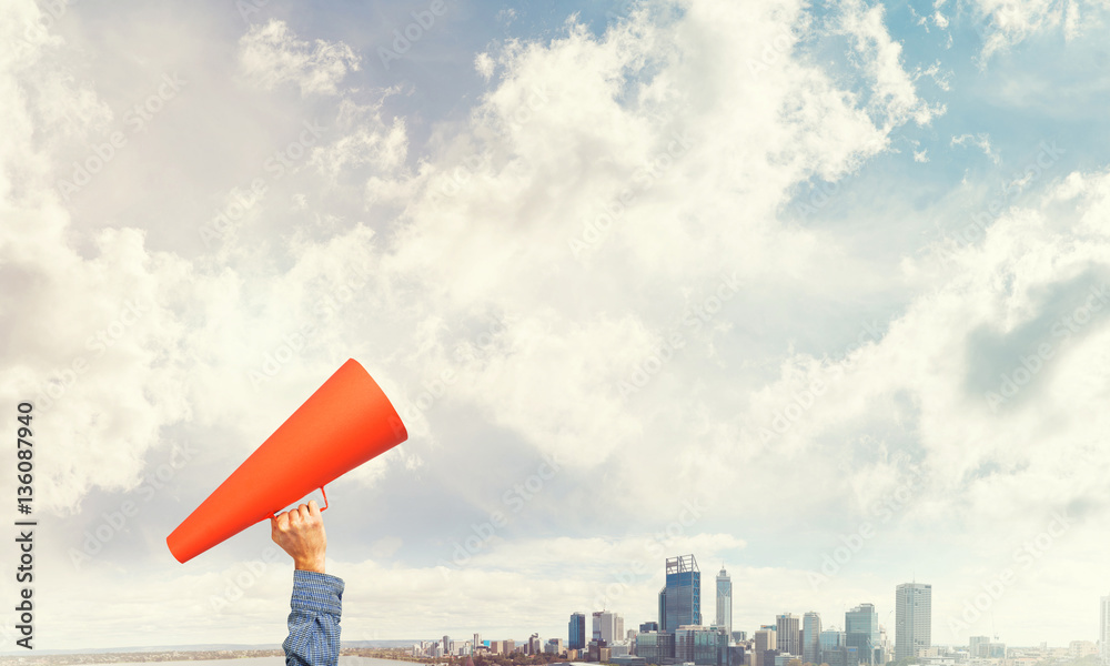 Hand of man holding red paper trumpet against cityscape background