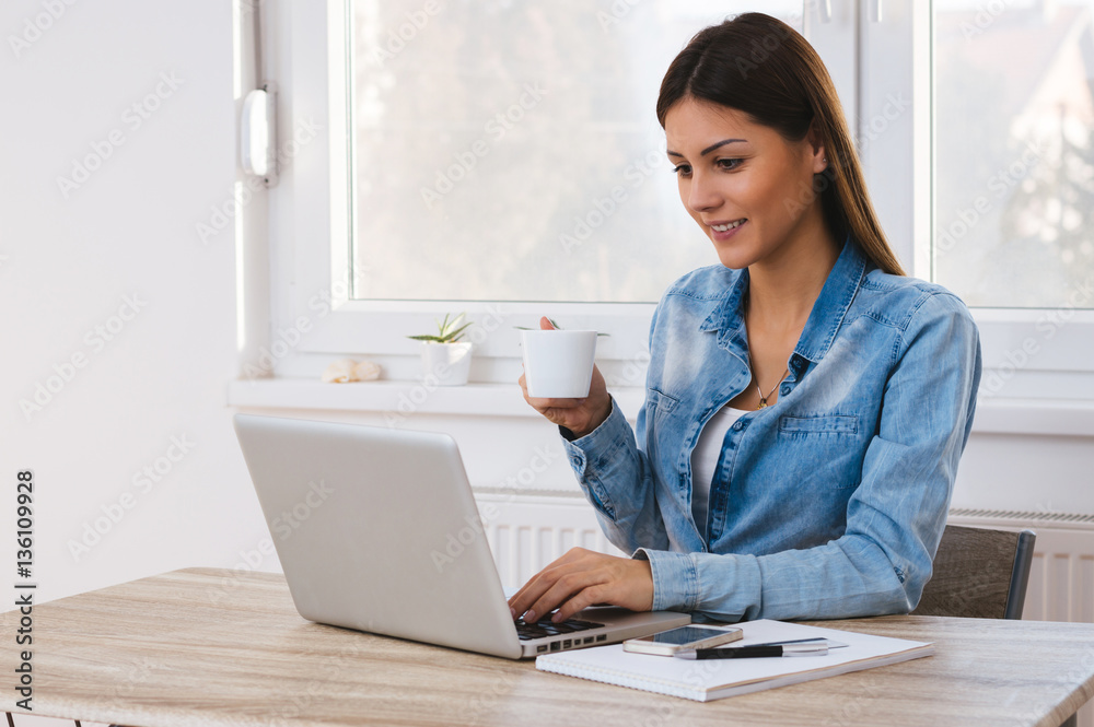 Young smiling woman at desk networking, drinking coffee