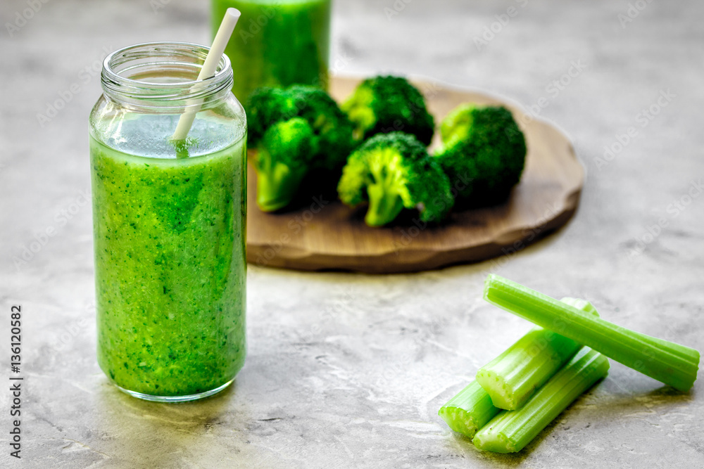 Green vegetable smoothie in glass at gray background