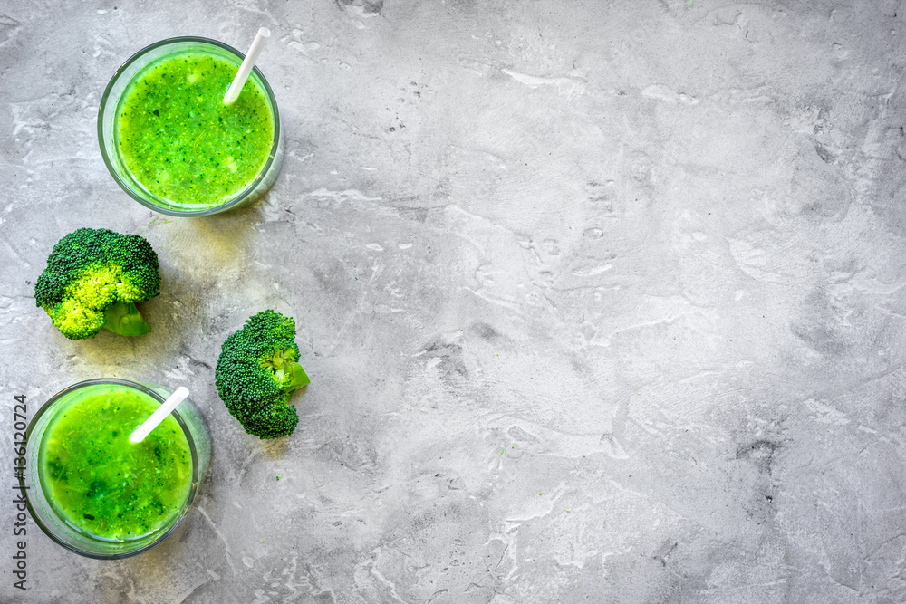 Green vegetable smoothie in glass at gray background top view