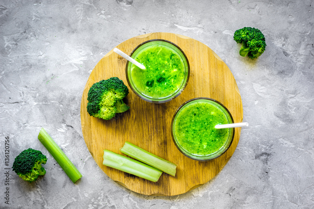 Green vegetable smoothie in glass at gray background top view