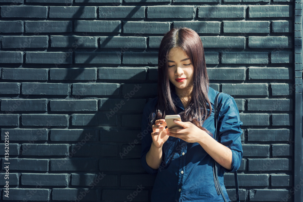 young asian woman standing outside against painted brick wall, u