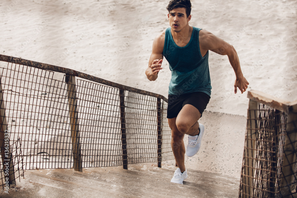 Fitness man running up the steps on beach