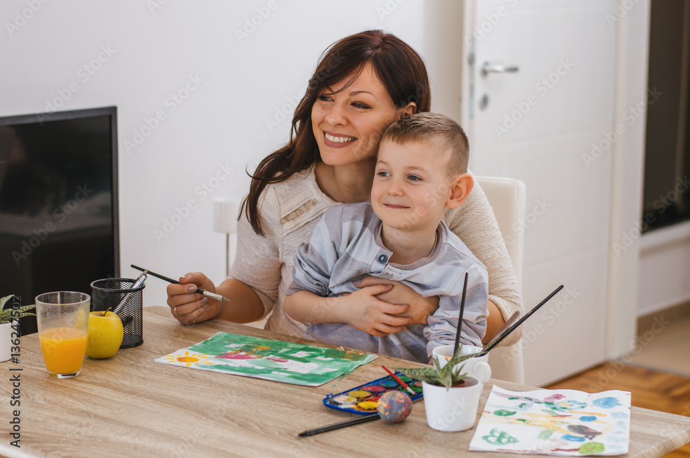 Joyful young mother and her little son having fun and painting o