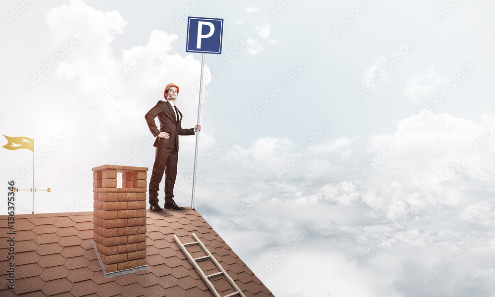 Young businessman with parking sign standing on brick roof. Mixe