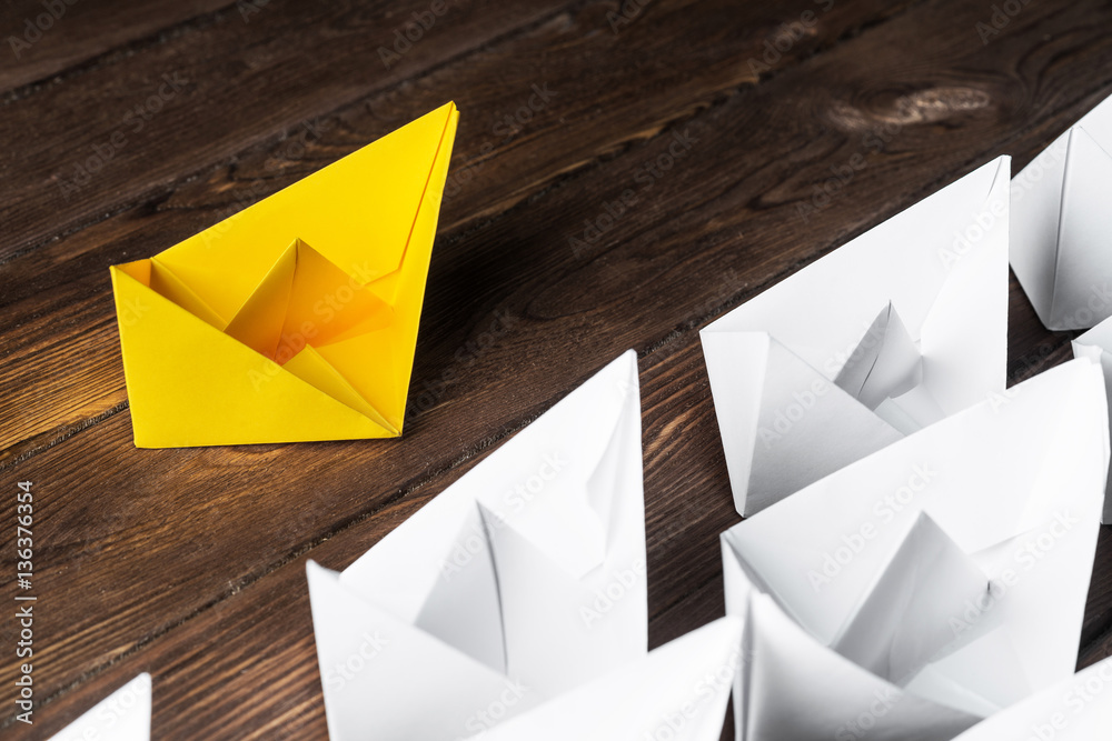 Business leadership concept with white and color paper boats on wooden table