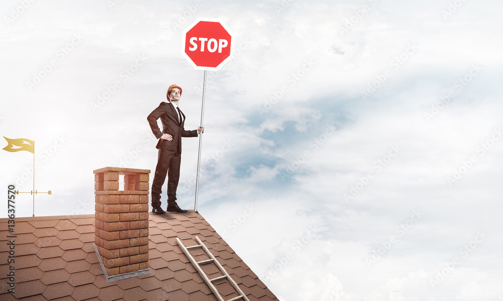 Caucasian businessman on brick house roof showing stop road sign