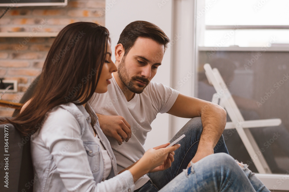 Couple relaxing and using a smart phone sitting on the floor indoors