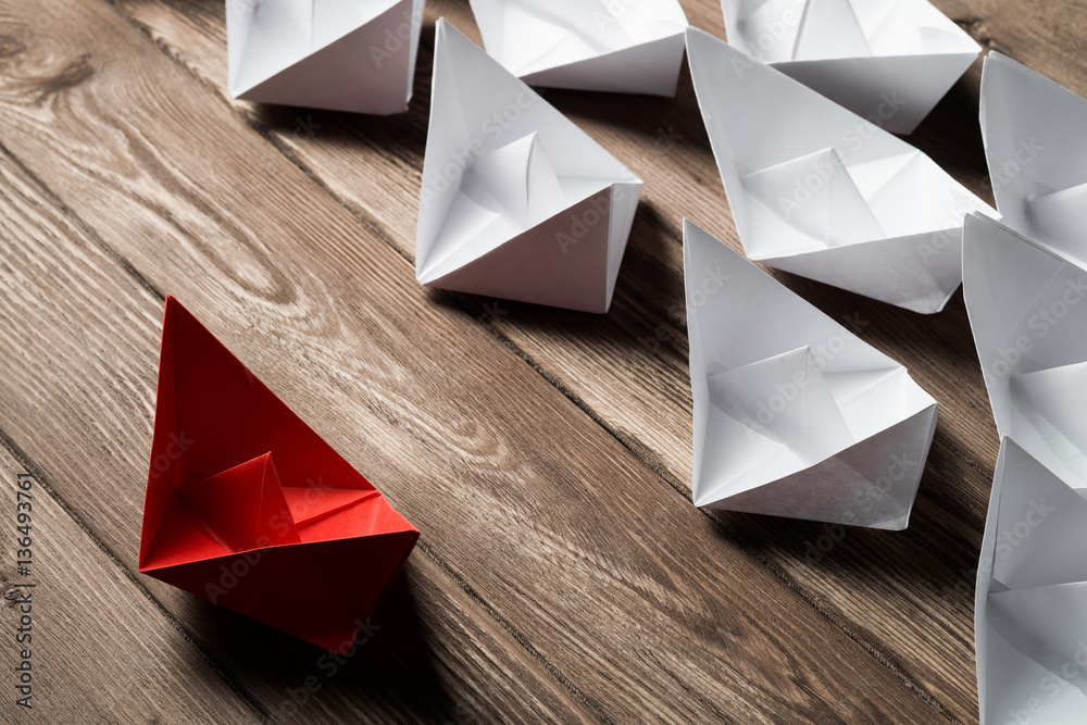 Business leadership concept with white and color paper boats on wooden table