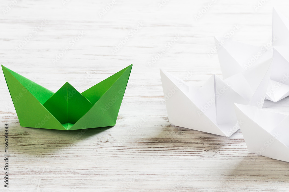 Business leadership concept with white and color paper boats on wooden table