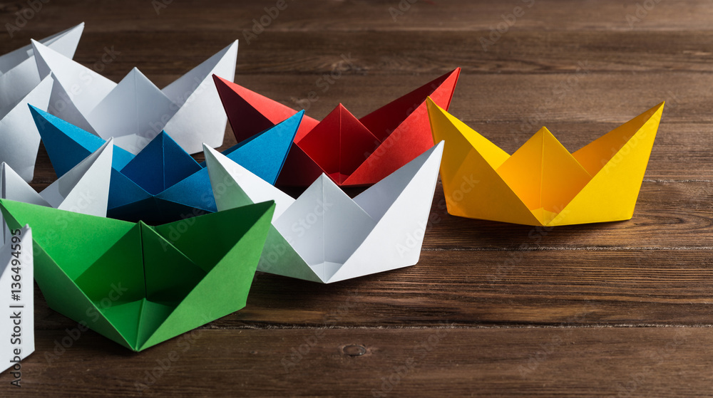 Business leadership concept with white and color paper boats on wooden table