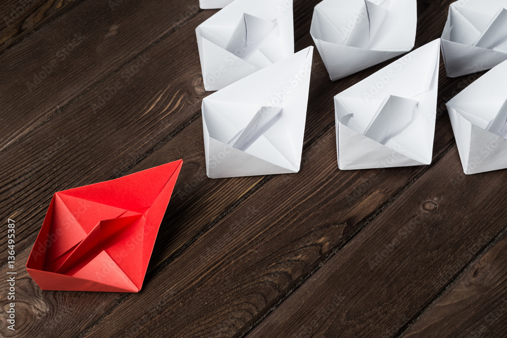 Business leadership concept with white and color paper boats on wooden table