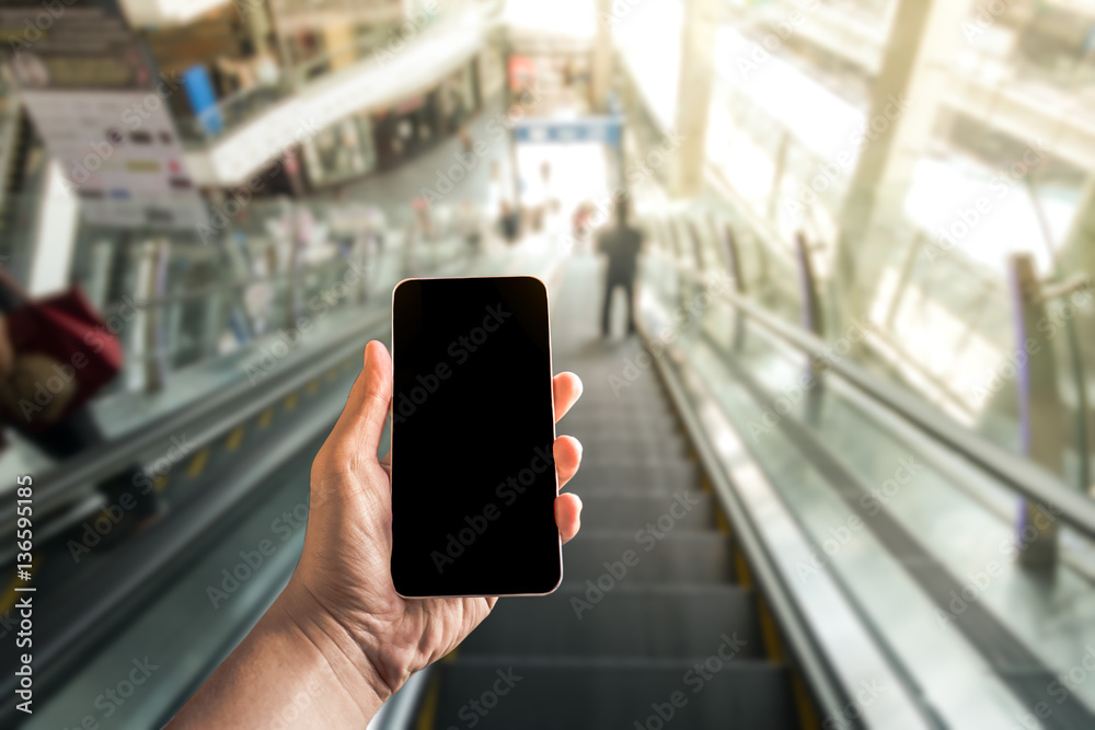 Mobile hold in hand with blur shopping mall in escalator