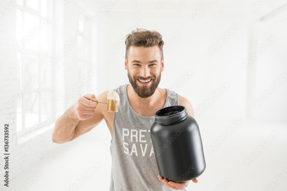 Athletic man in sportswear pouring with scooper protein powder in the white gym interior