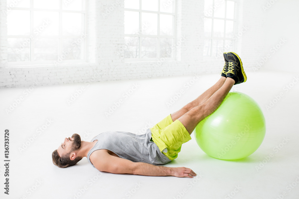 Handsome man exercising with fitball in the white gym interior